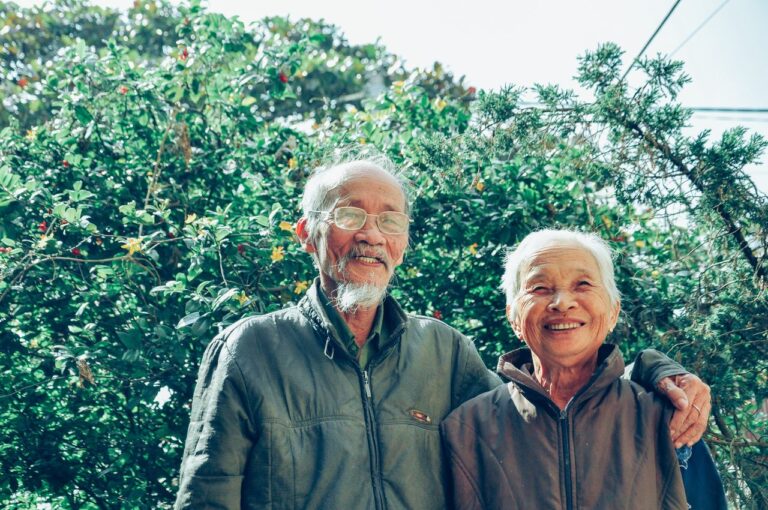 A happy elderly couple smiles warmly outdoors against a vibrant green background.