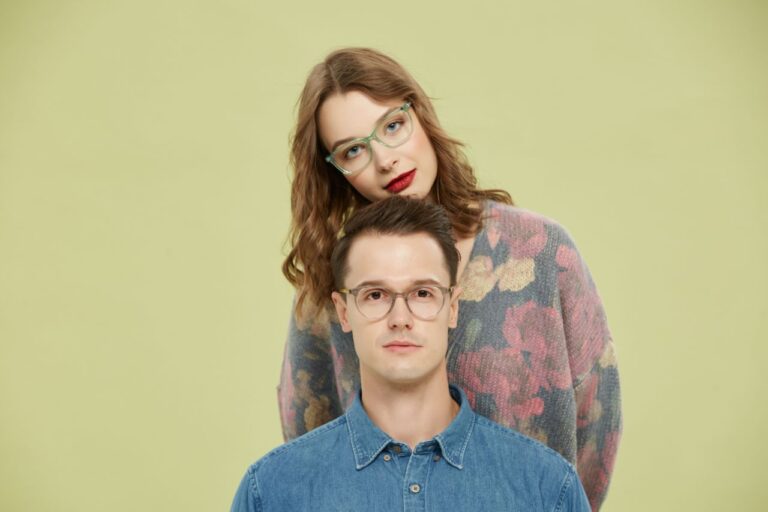 A fashionable couple sporting trendy eyeglasses poses against a light background.
