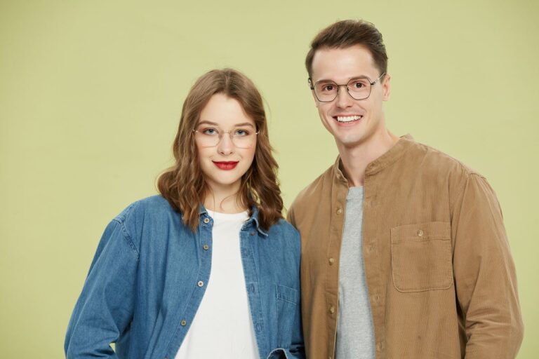 Smiling couple in trendy eyewear and casual clothing against a neutral background.