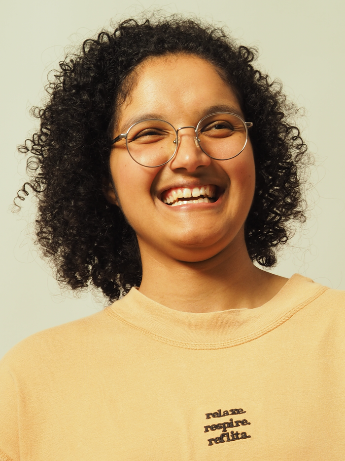 Cheerful individual with curly hair and glasses laughing, exuding joy.
