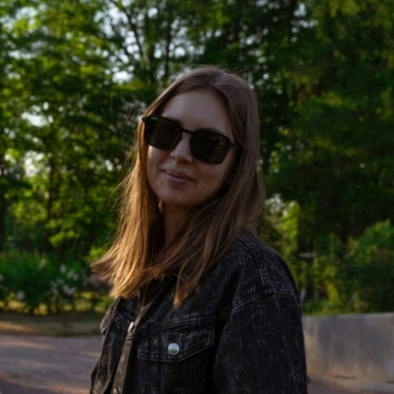 A woman smiles while wearing sunglasses outdoors