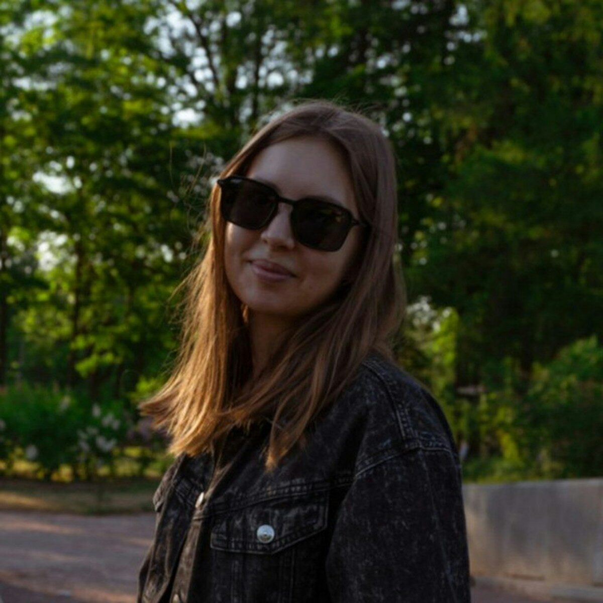 A woman smiles while wearing sunglasses outdoors