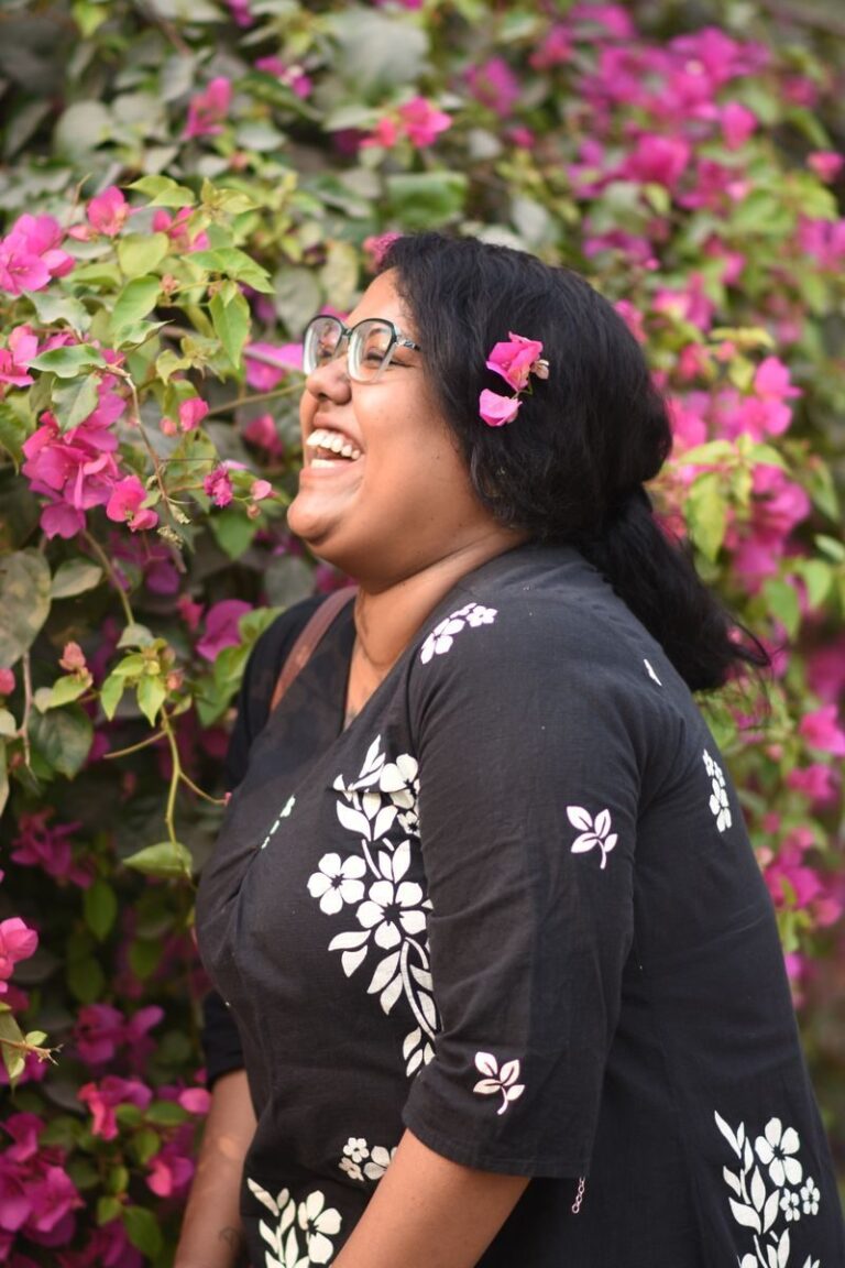 A woman laughing joyfully near vibrant bougainvillea blooms, embracing nature's beauty.
