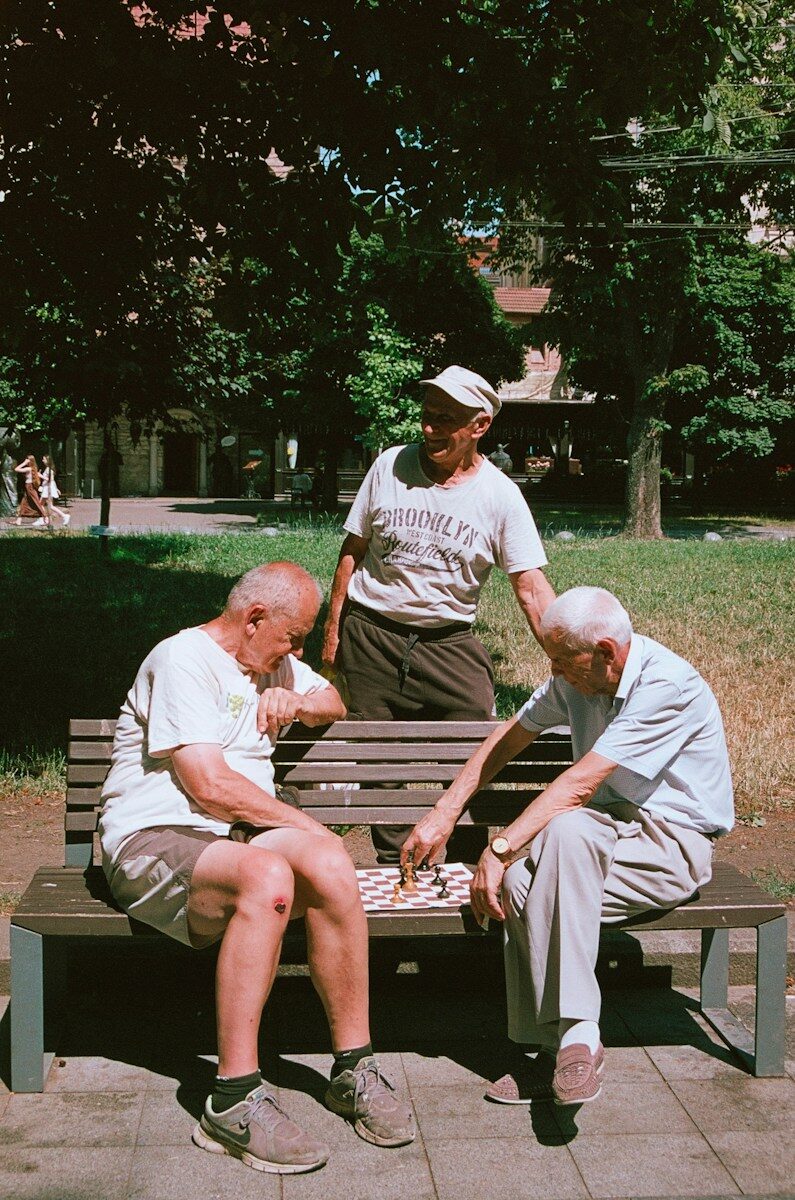 Three older men play checkers on a park bench